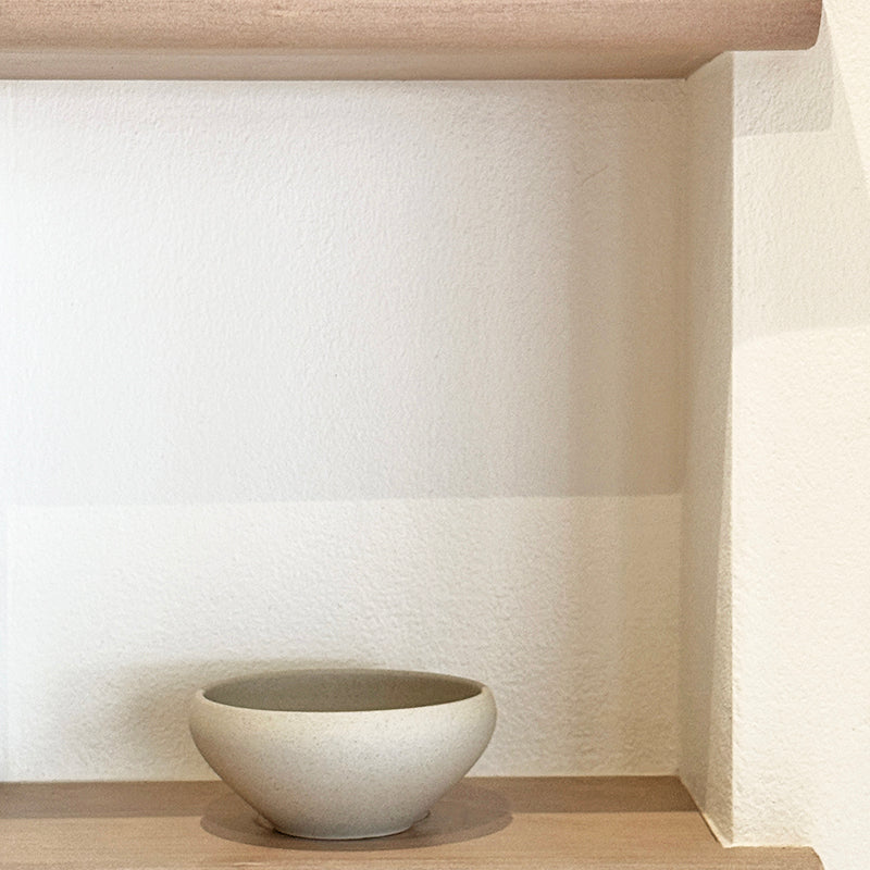 Stoneware bowl on wooden shelf with white wall