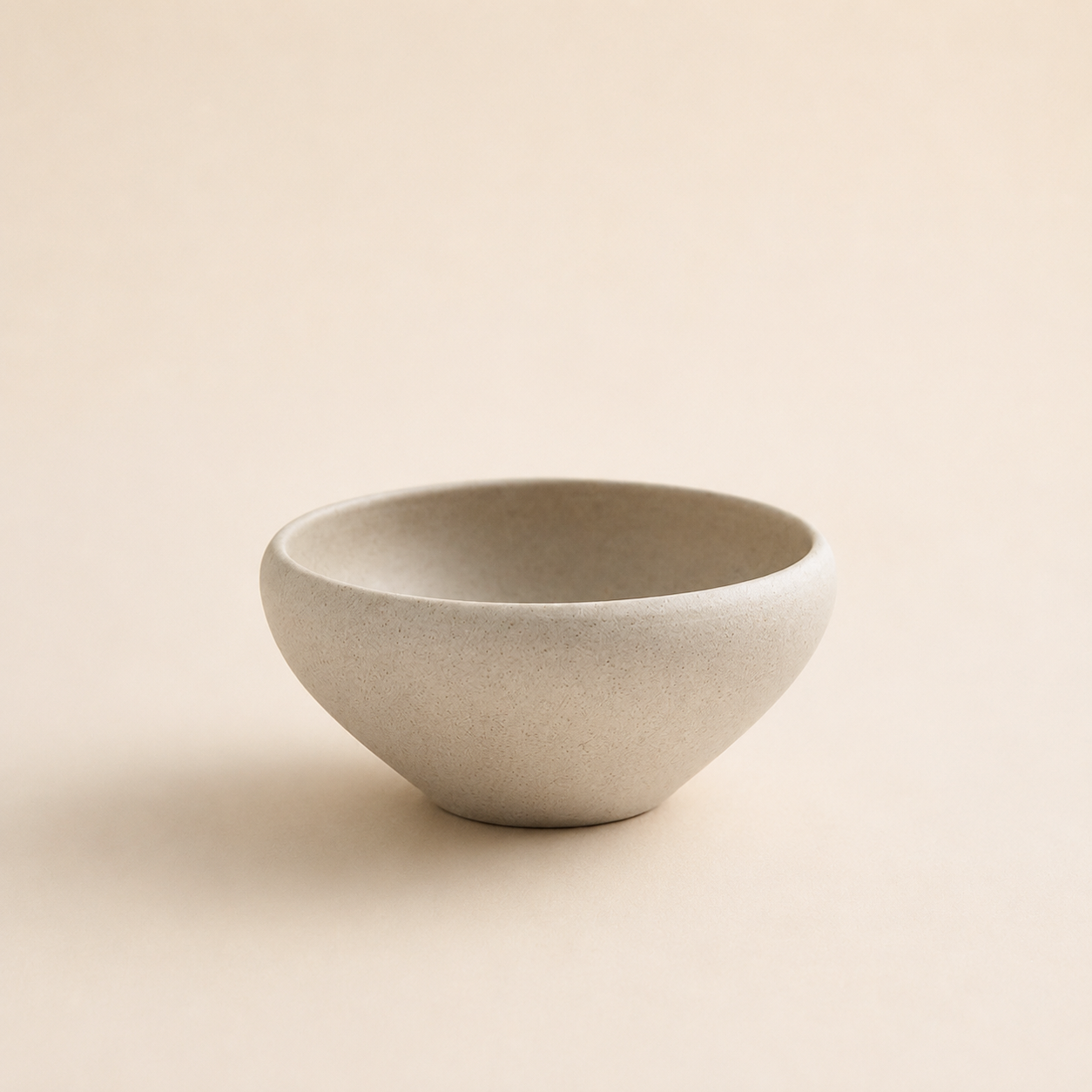 Small speckled cream stoneware bowl on a neutral background