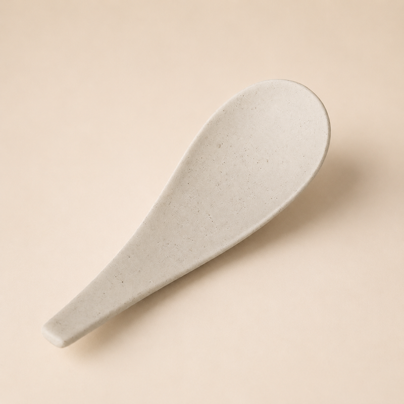 Cream speckled stoneware serving spoon on a neutral background