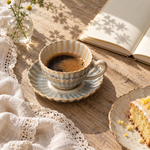 Blue Grey coffee cup and saucer with a notebook and flowers on an oak table