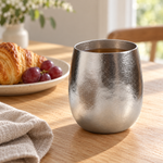 Pebble titanium cup with tea beside a breakfast plate on a light oak table