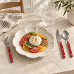 Red matte riveted flatware beside a tomato and burrata salad